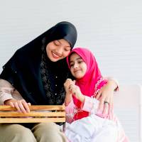 Muslim mother and her daughter are enjoin with cosmetic activity together in the room with white background and copy space.